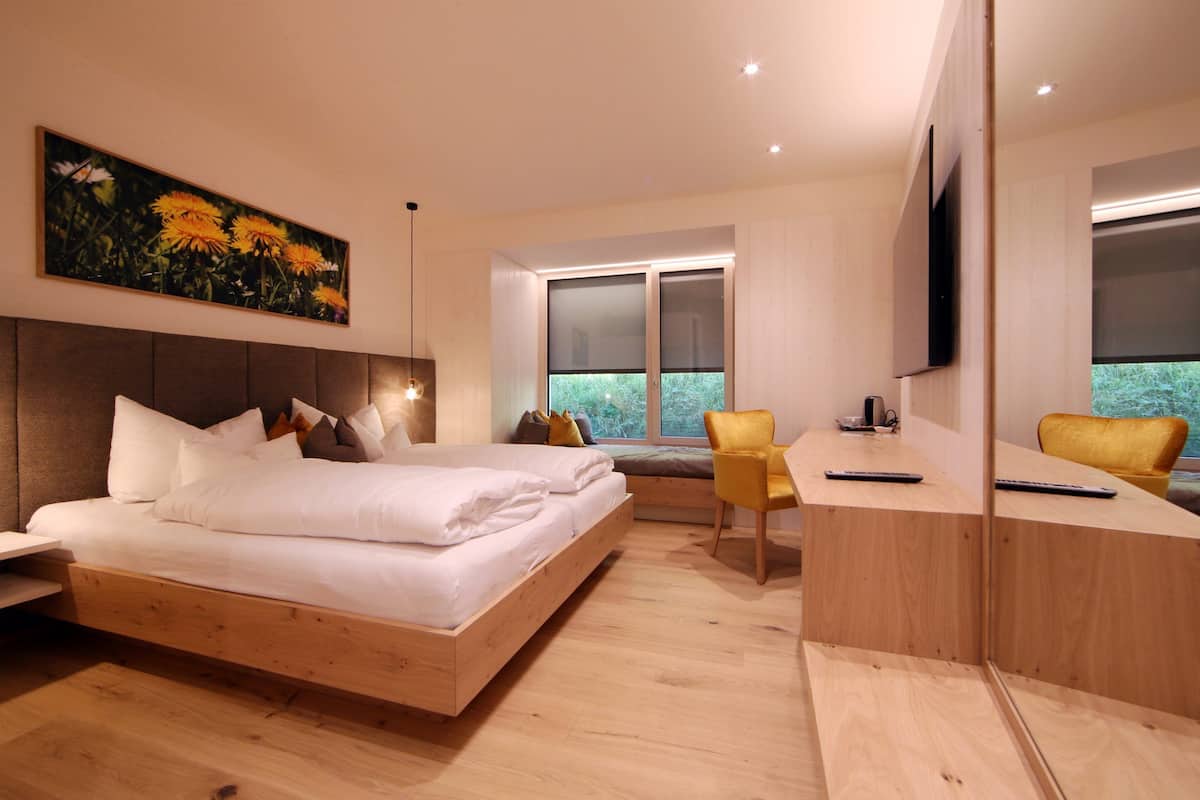 Un dormitorio moderno con una cama de madera, un escritorio, dos sillas, un ventanal grande y un cuadro en la pared.
