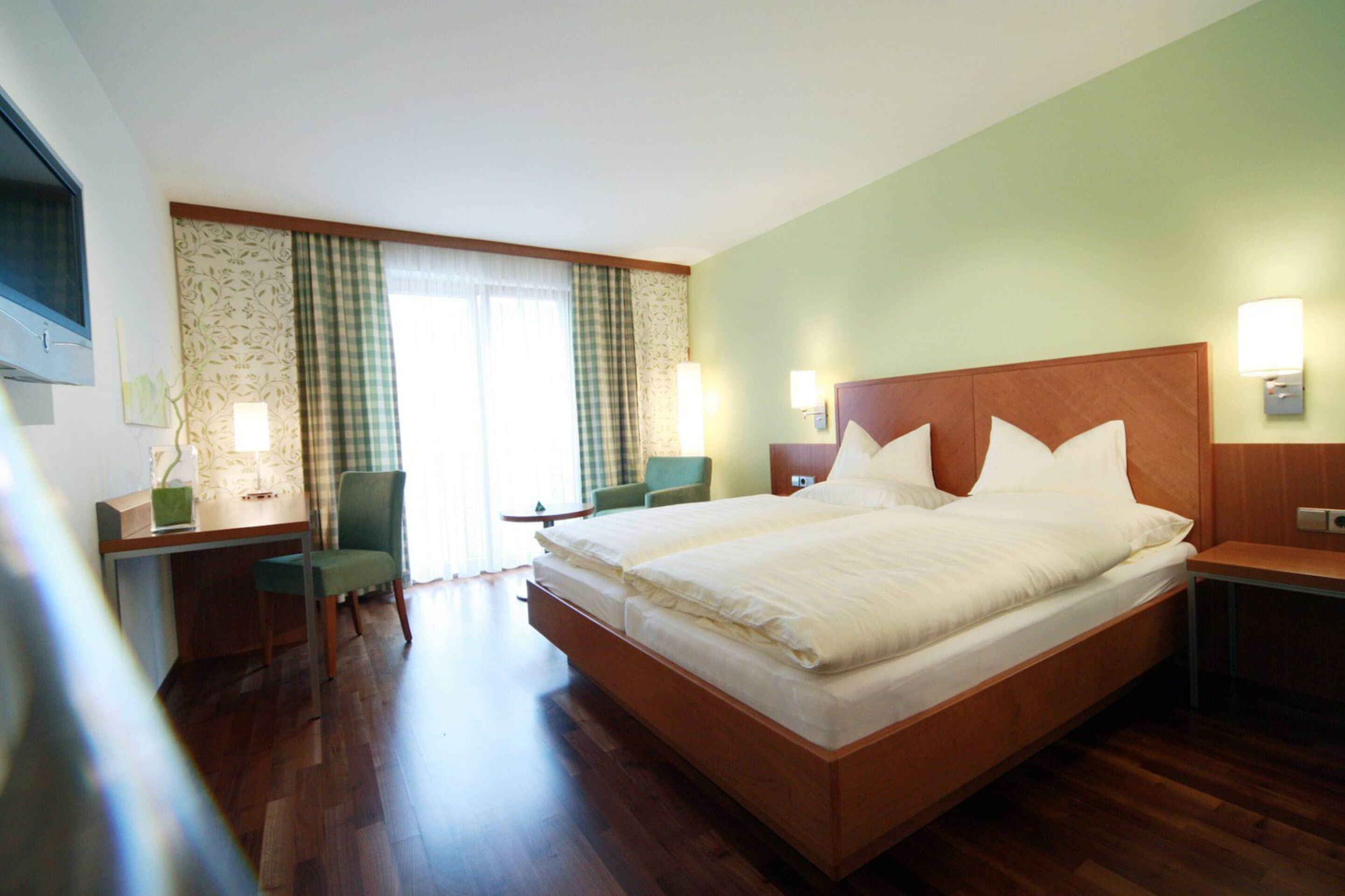 Una habitación de hotel con una cama grande, un escritorio, una silla y una ventana con cortinas.