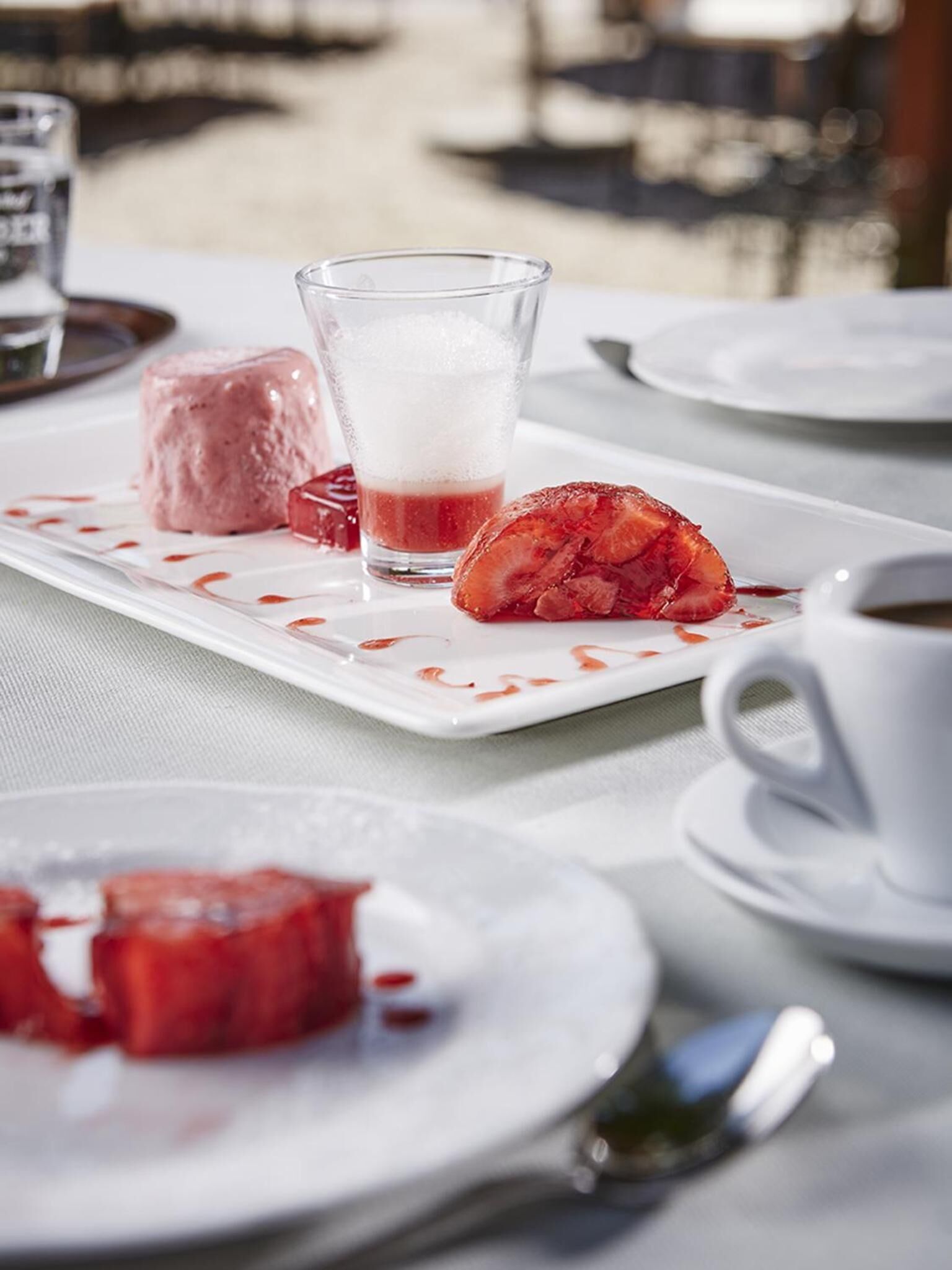 A table with a dessert plate containing a pink dessert, a glass of a red beverage, and a white cup.