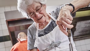 Una persona mayor cortando carne en una tabla de cocina.