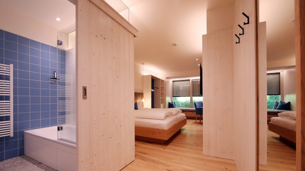 Un dormitorio moderno con una cama grande, una sala de estar separada y un baño con bañera y azulejos azules.