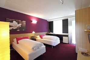 Ein Hotelzimmer mit zwei Betten, einem Schreibtisch, einem Stuhl, einer Lampe und einem Fenster.