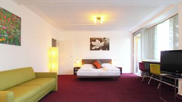 Une chambre d’hôtel avec un lit, un canapé vert, une télévision et un tableau au mur.