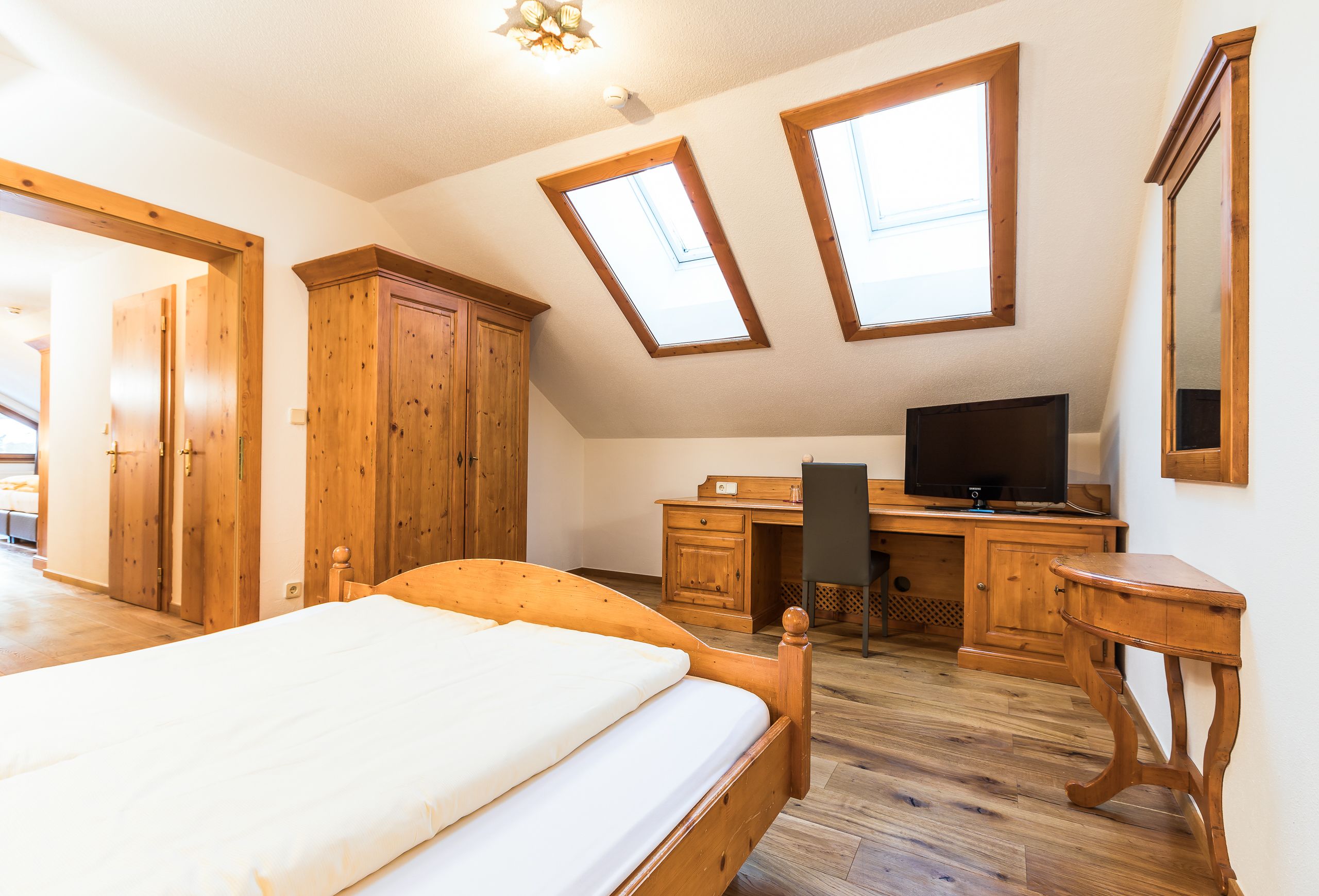 Quarto com cama, guarda-roupa de madeira, escrivaninha, televisão e claraboias.