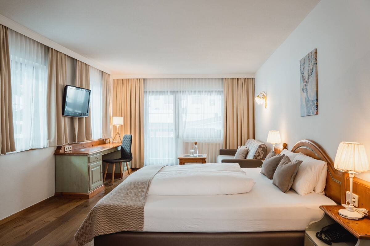 A hotel room with a large bed, a desk with a chair, a television, and two bedside lamps.