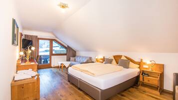 Quarto com cama grande, mesas de cabeceira de madeira, escrivaninha com abajur e janela com cortinas.
