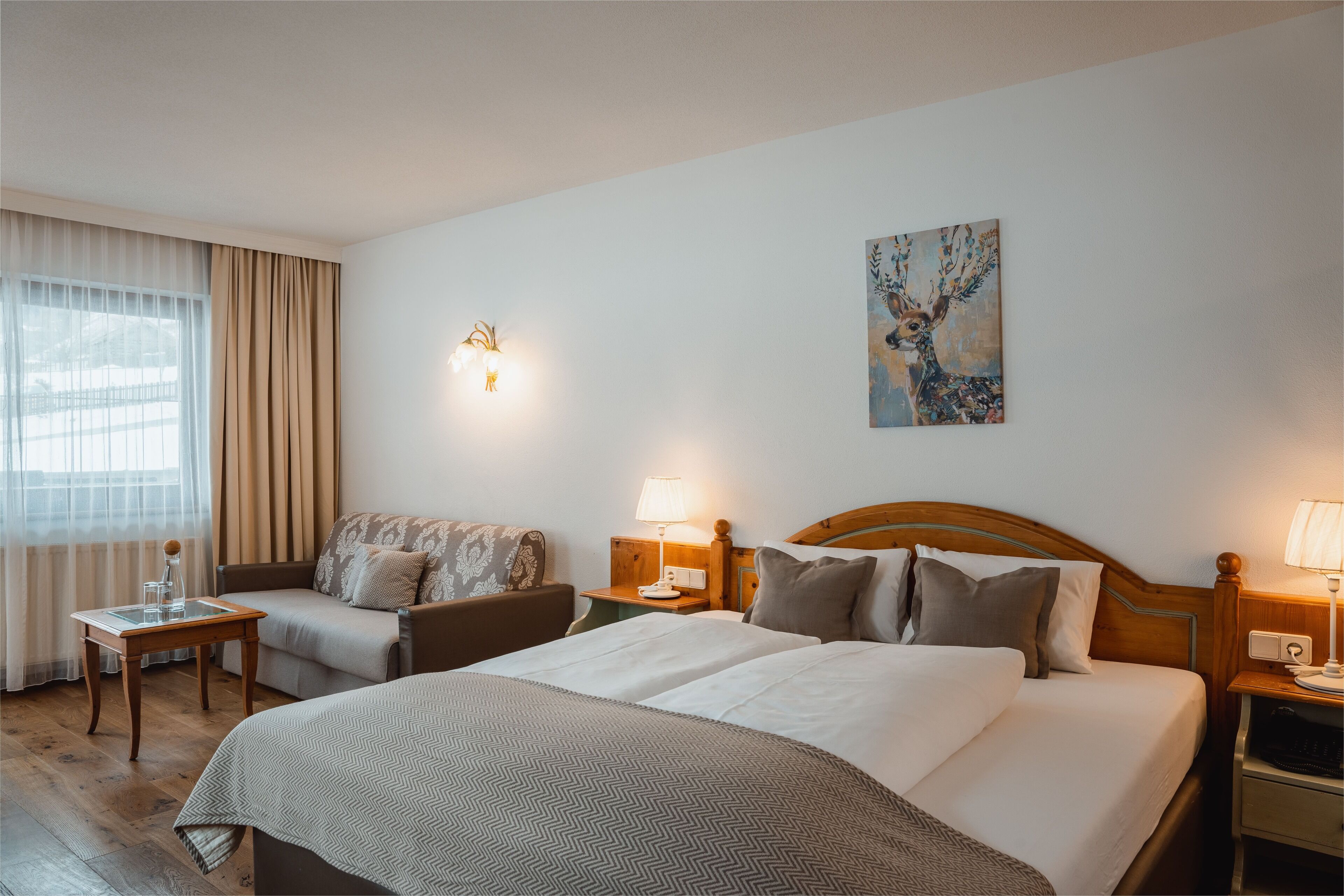 A hotel room with a large bed, a sofa, a small table, a lamp, and a painting on the wall.
