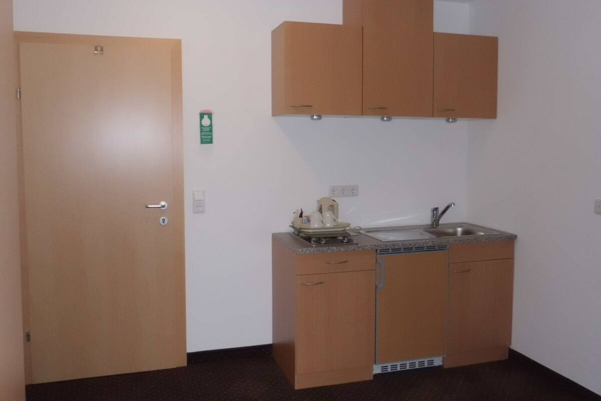 A compact kitchenette with a sink, a coffee maker, and a microwave. There is a door with a lock and a small window.