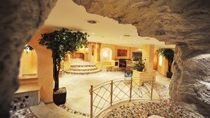A lobby with a central staircase, a large tree, and a stone wall. - Sporthotel Kirchler (Tux)