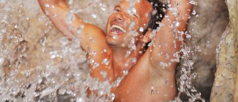A person submerged in water, with arms raised, in a rocky environment.
