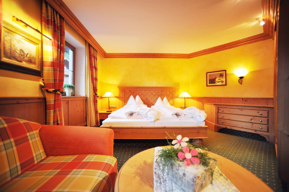 A hotel room with a bed, a sofa, a nightstand, and a wall-mounted lamp.