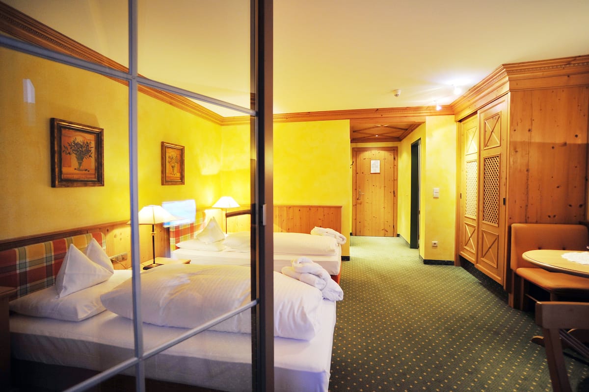 A hotel room with two beds, a dining area, and a wooden wardrobe.