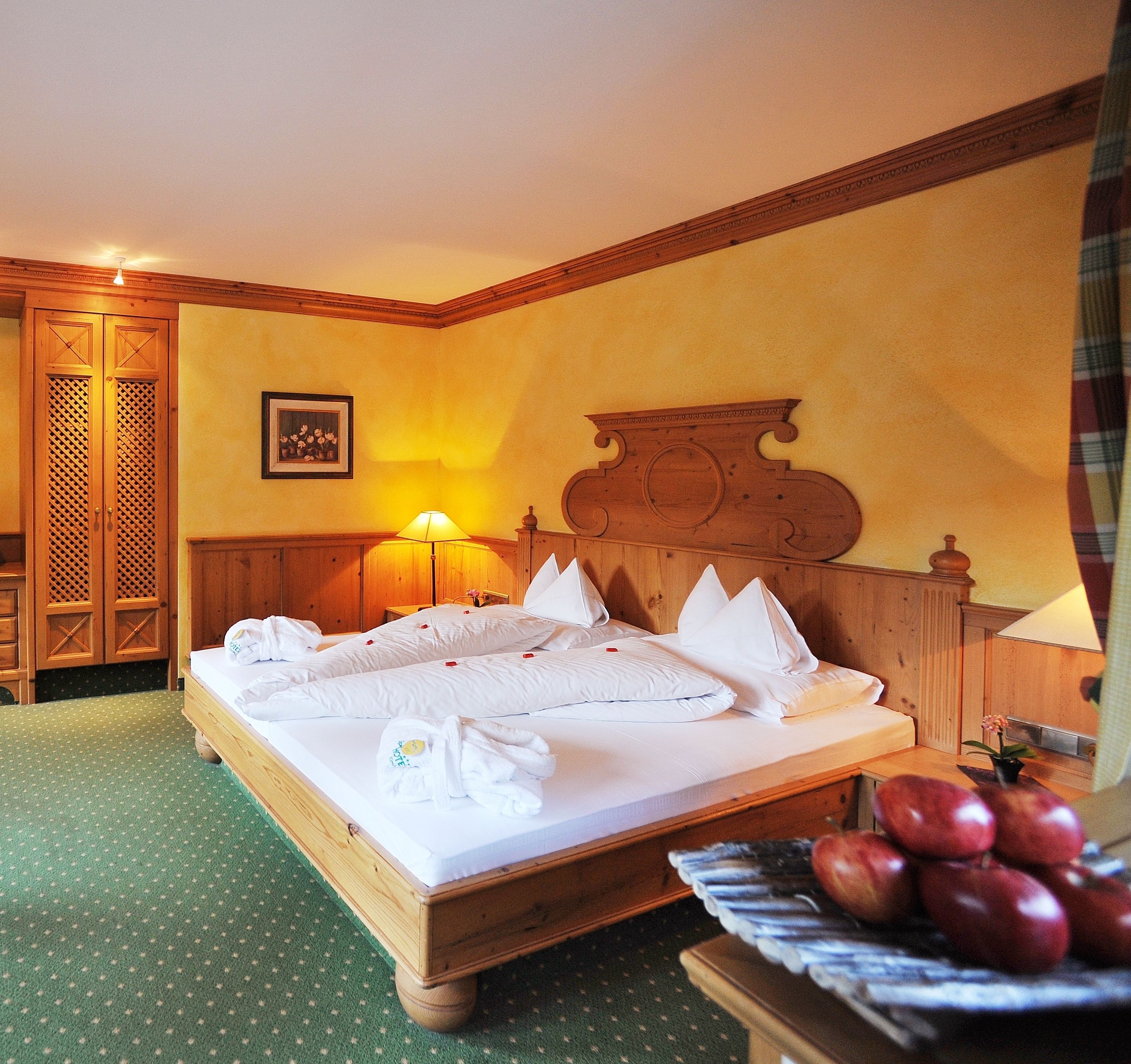 Habitación de hotel con una cama de madera, alfombra verde, armario de madera y cabecero de madera.