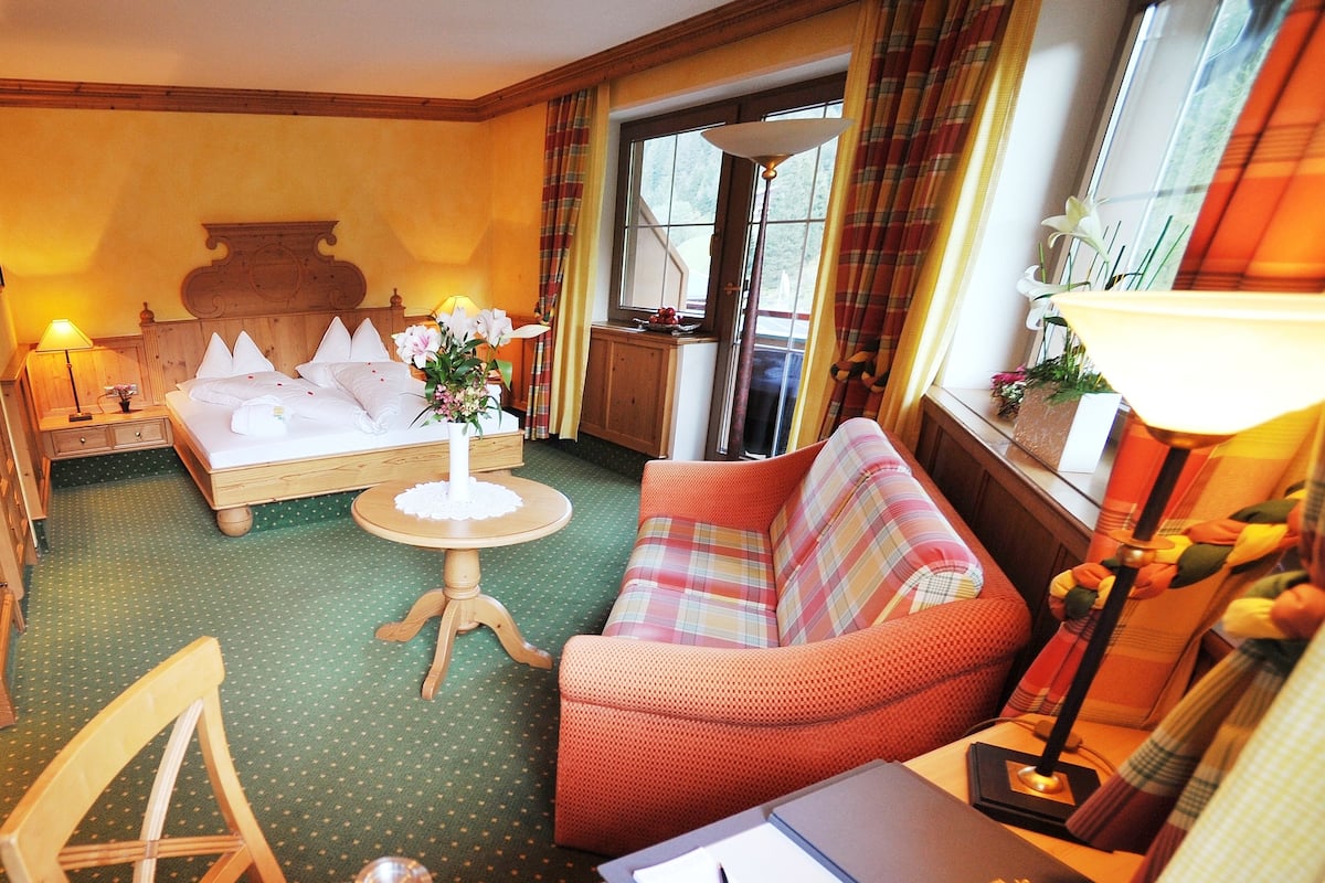 A hotel room with a bed, a sofa, a small round table, a laptop, and a lamp.