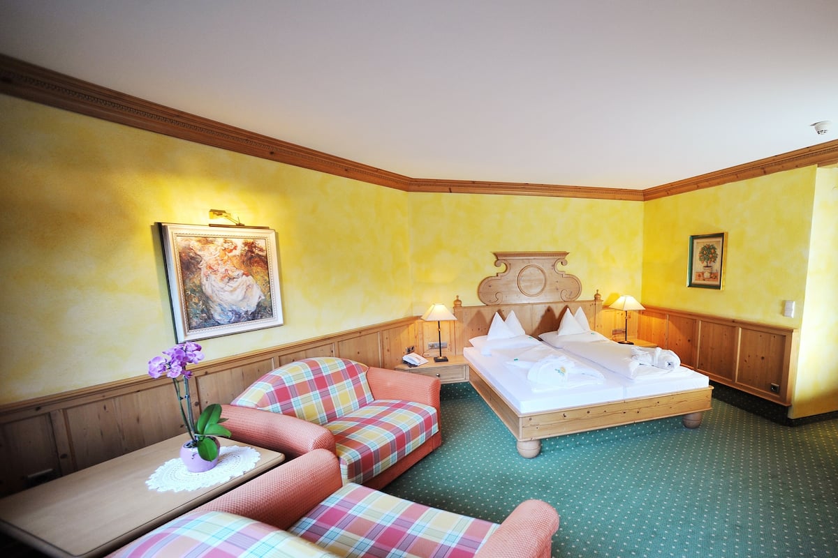 A hotel room with a bed, two sofas, a small table with a vase of flowers, and two wall-mounted lamps.