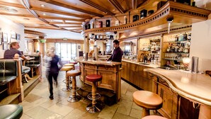A bar area with wooden bar stools, a bartender, and a well-stocked liquor shelf. - Sporthotel Kirchler (Tux)