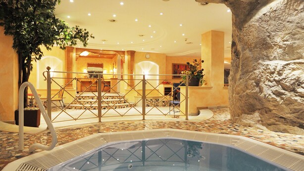 A hot tub in a room with a rock-like ceiling, a staircase, and a plant. - Sporthotel Kirchler (Tux)