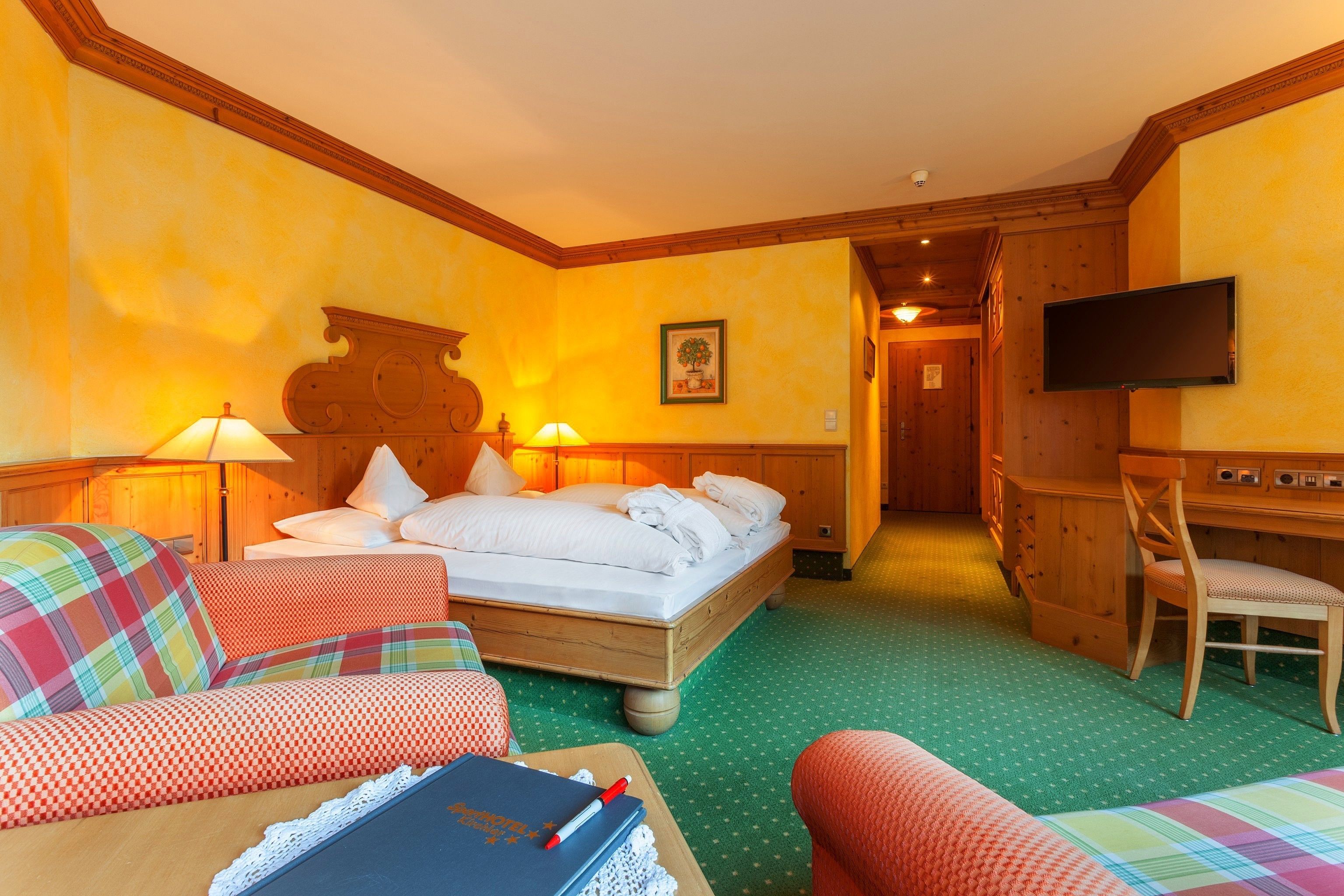 A hotel room with a bed, two chairs, a desk, and a television.
