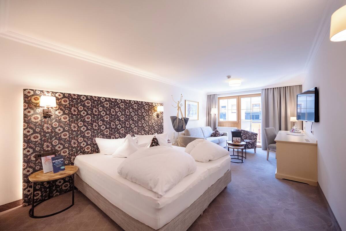 A hotel room with a large bed, a desk, a chair, a sofa, and a TV.