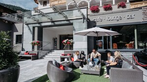 An outdoor seating area with wicker furniture and a glass railing, a cafe/lounge bar sign, and a staircase leading to an upper level. - Hotel Salzburger Hof (Altenmarkt im Pongau)