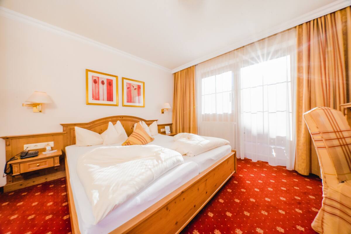 A hotel room with a wooden bed, two bedside tables, a nightstand, a lamp, and a chair.