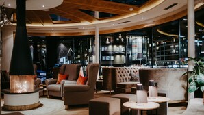 A modern lounge area with sofas, a fireplace, and a bar with a view of the city. - Hotel Salzburger Hof (Altenmarkt im Pongau)