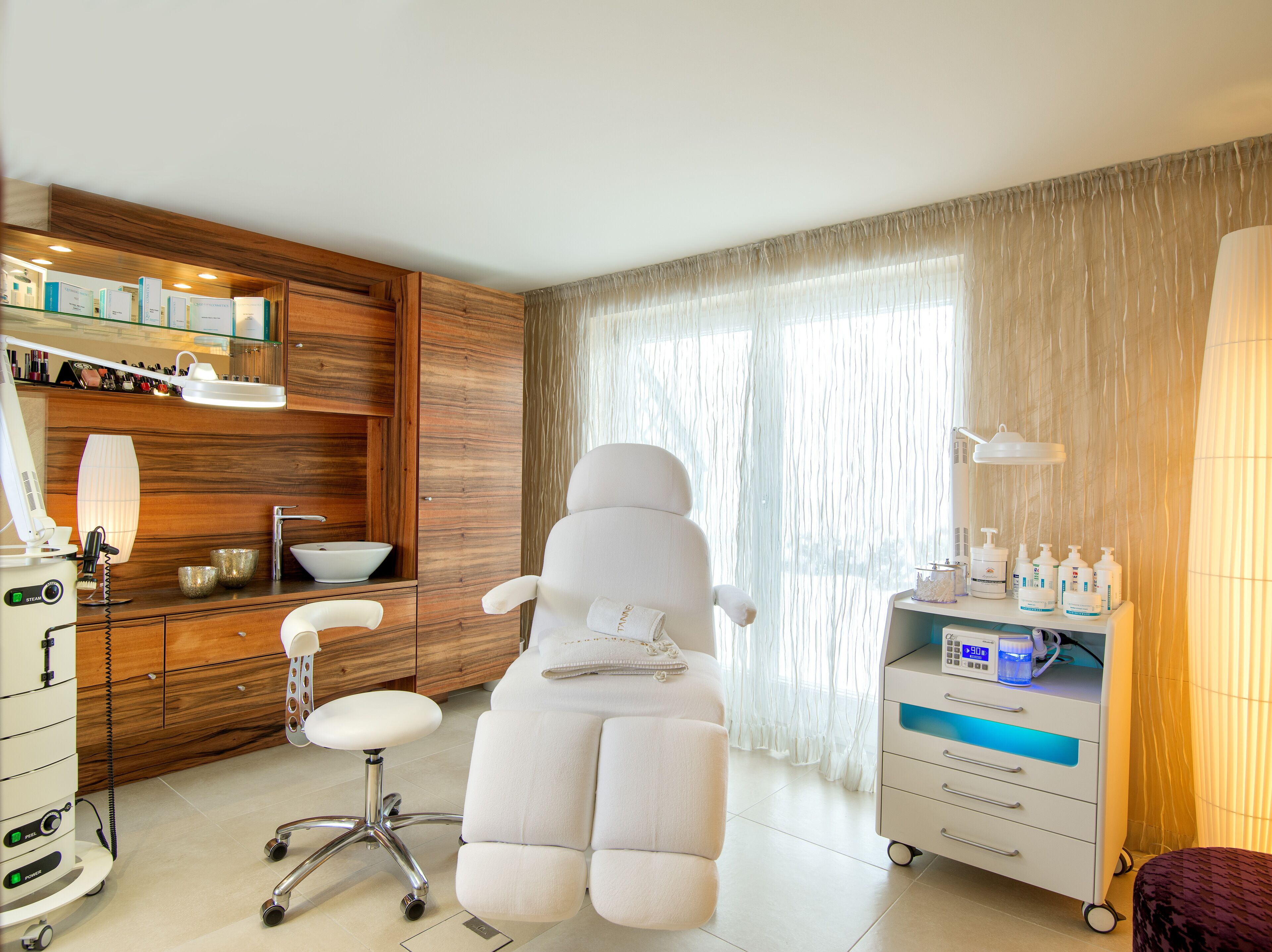 A modern spa room with a massage chair, a vanity with a sink, and a cabinet with various toiletries.