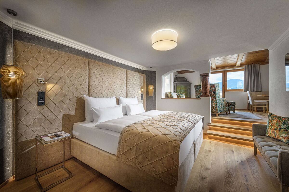 A modern hotel room with a large bed, a small table, a sofa, and a staircase leading to an upper level.