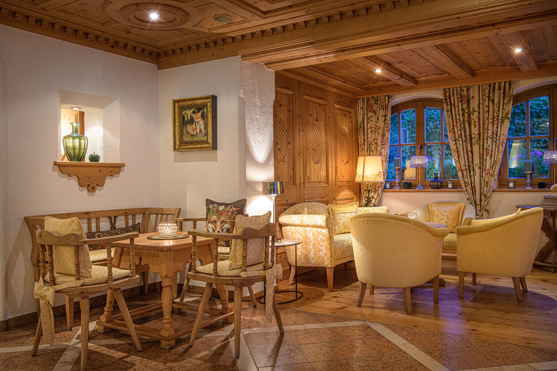 A traditional room with wooden furniture, a fireplace, and a view of greenery through large windows.