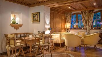A traditional room with wooden furniture, a fireplace, and a view of greenery through large windows.