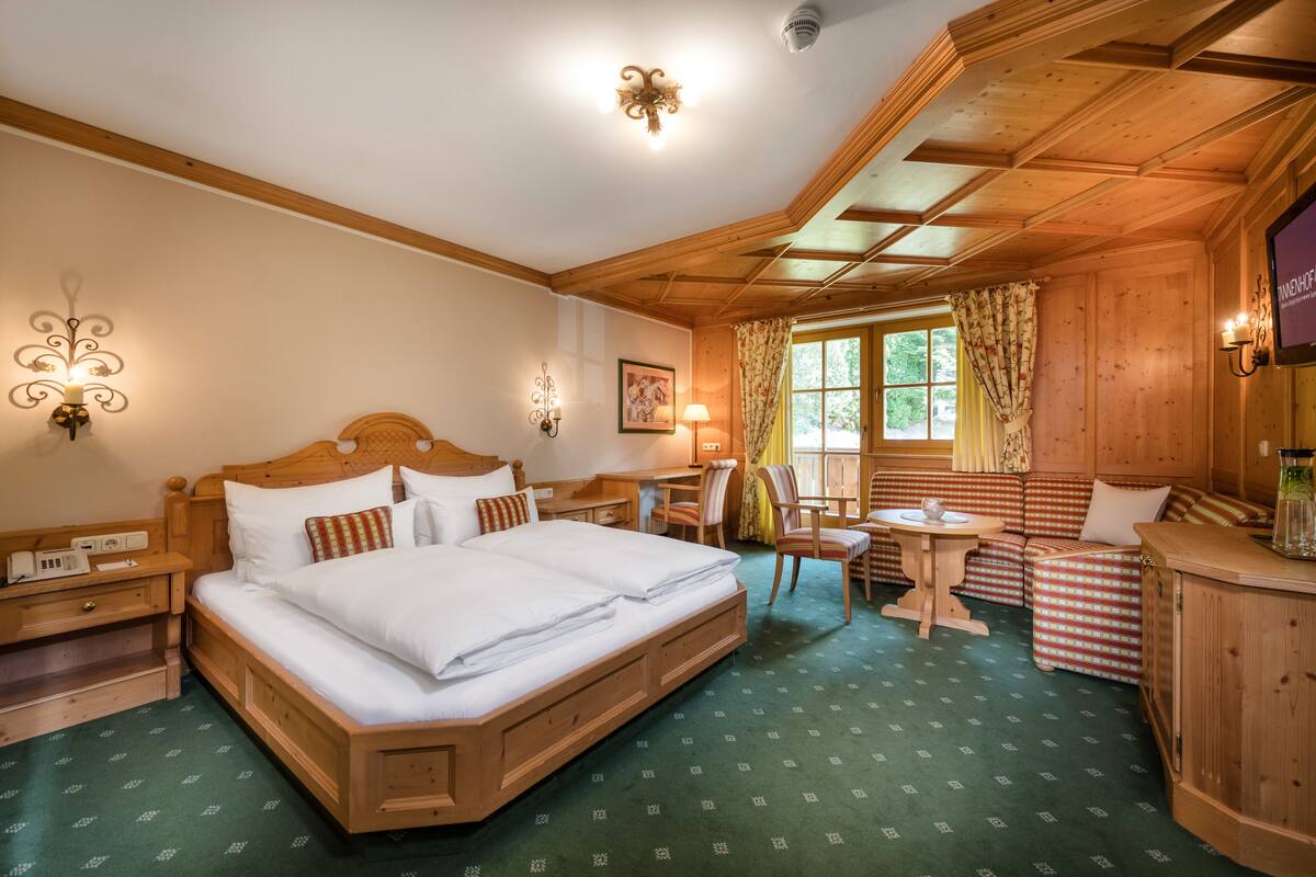 A wooden room with a large bed, a small table, a chair, and a sofa.