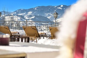 A snow-covered outdoor seating area with wicker chairs and tables, overlooking a mountainous landscape.