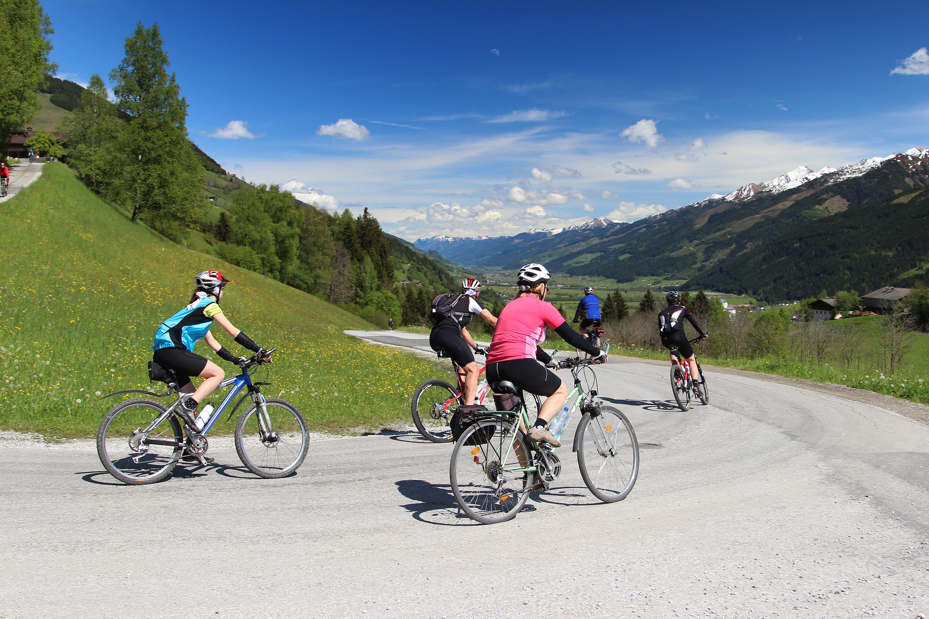 Un grupo de ciclistas en una carretera pavimentada con un paisaje montañoso al fondo.