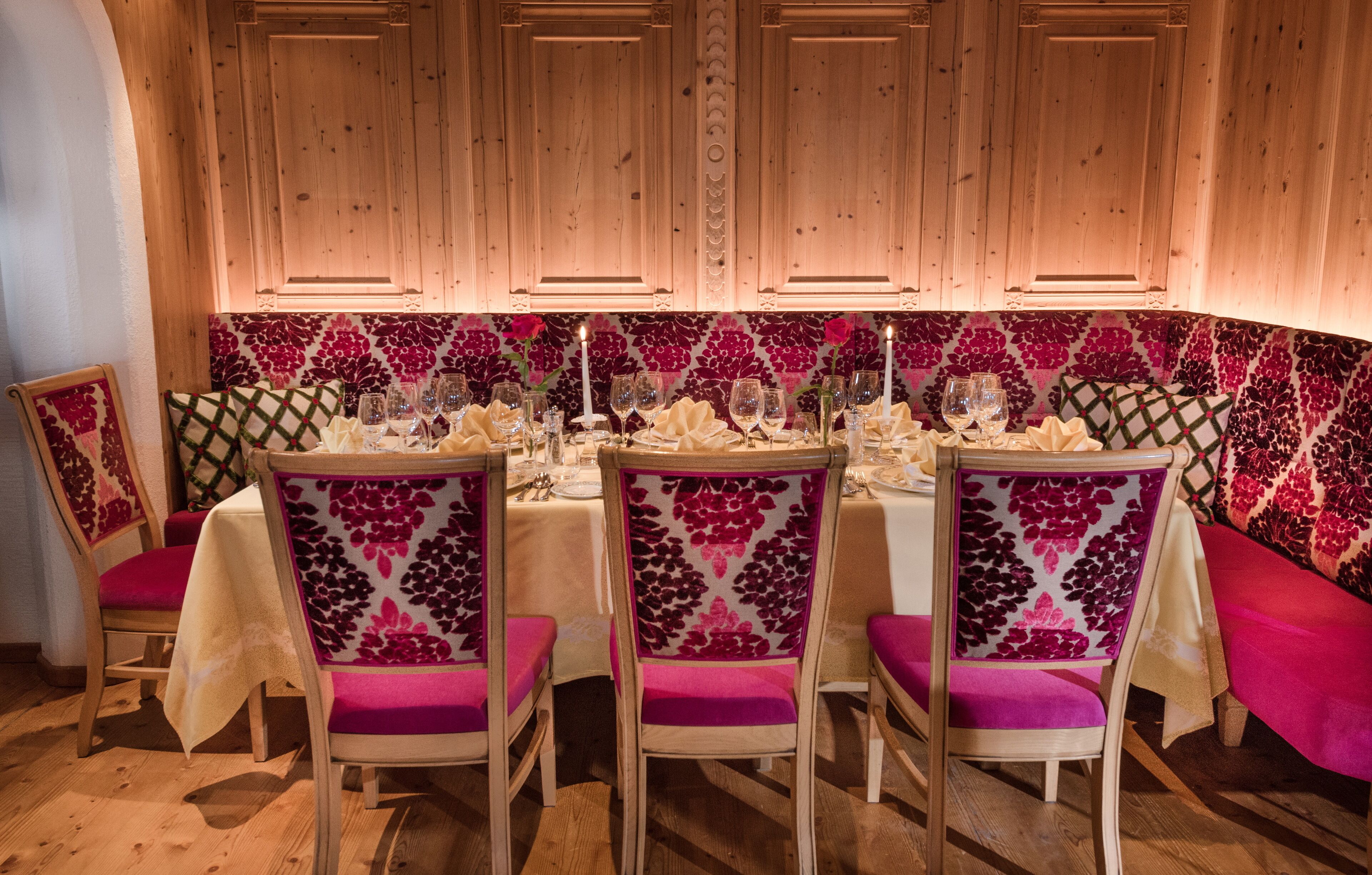 A dining area with wooden paneling, floral wallpaper, and pink upholstered chairs.