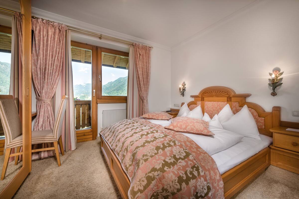 A bedroom with a wooden bed, a chair, a nightstand, and a window with curtains.