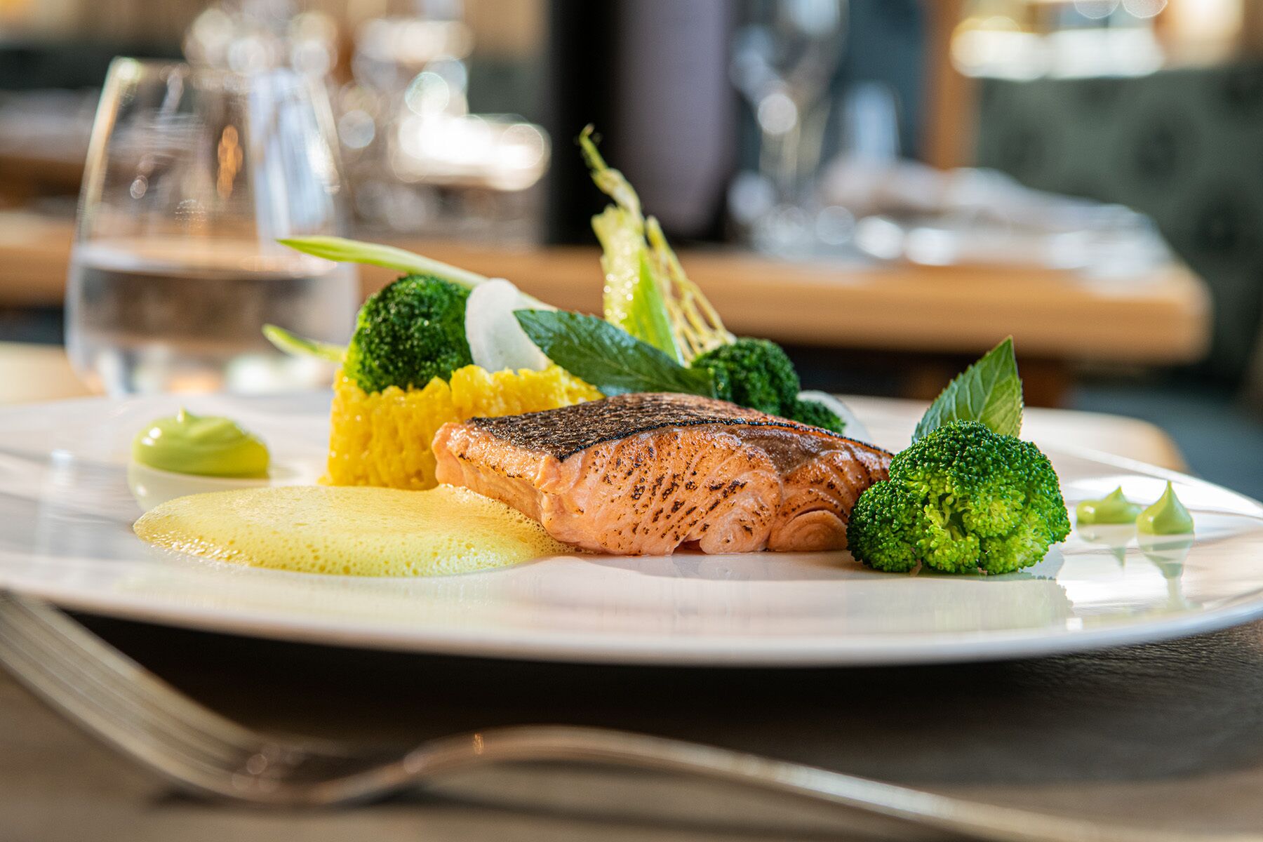 A plate with grilled salmon, broccoli, and a yellow vegetable, possibly a potato, on a white plate.