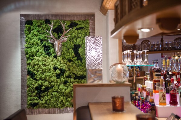A bar area with a green moss wall, a deer head decoration, and a variety of liquor bottles.