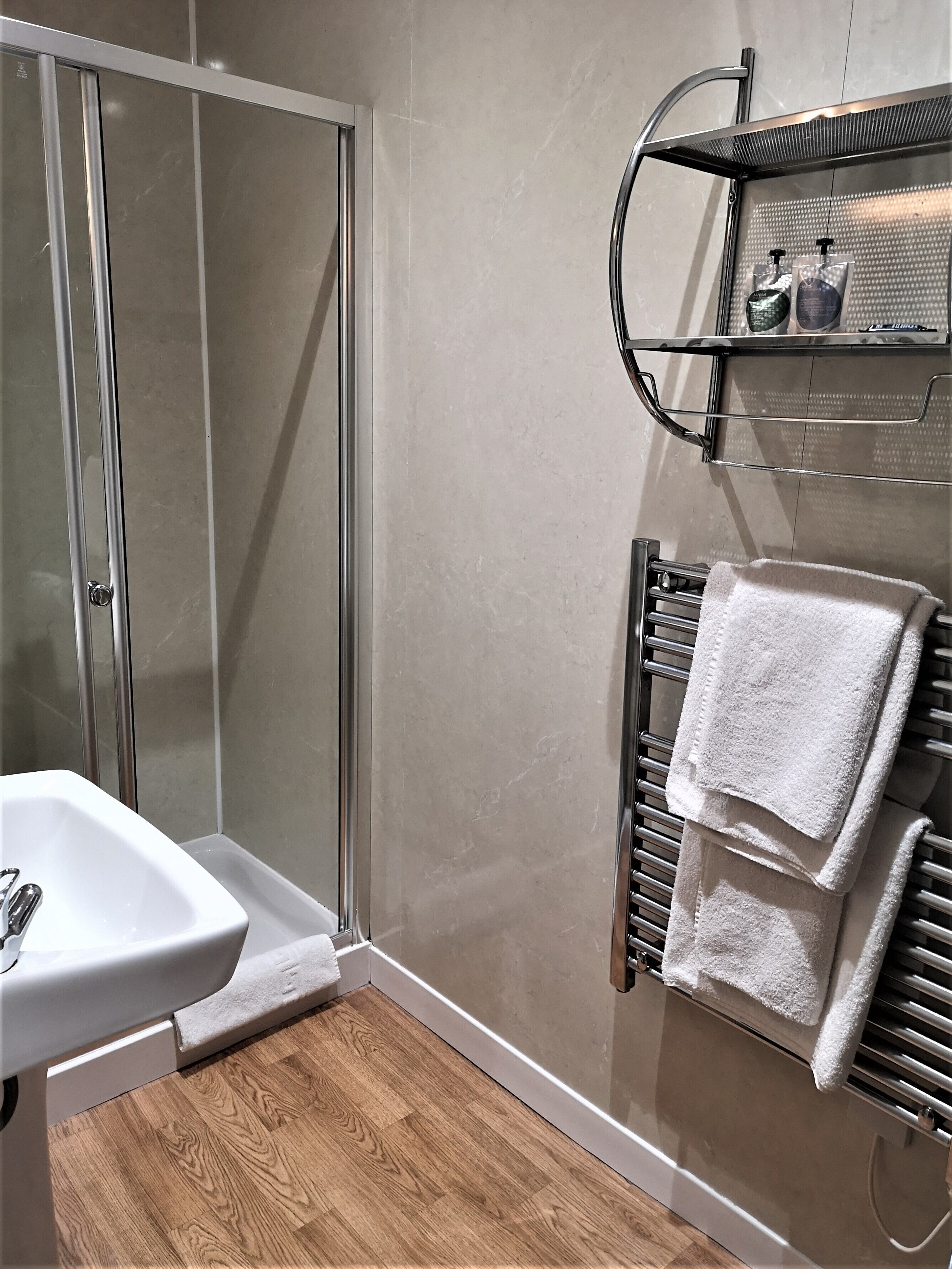 A modern bathroom with a glass shower enclosure, a white sink, and a towel rack with two towels.