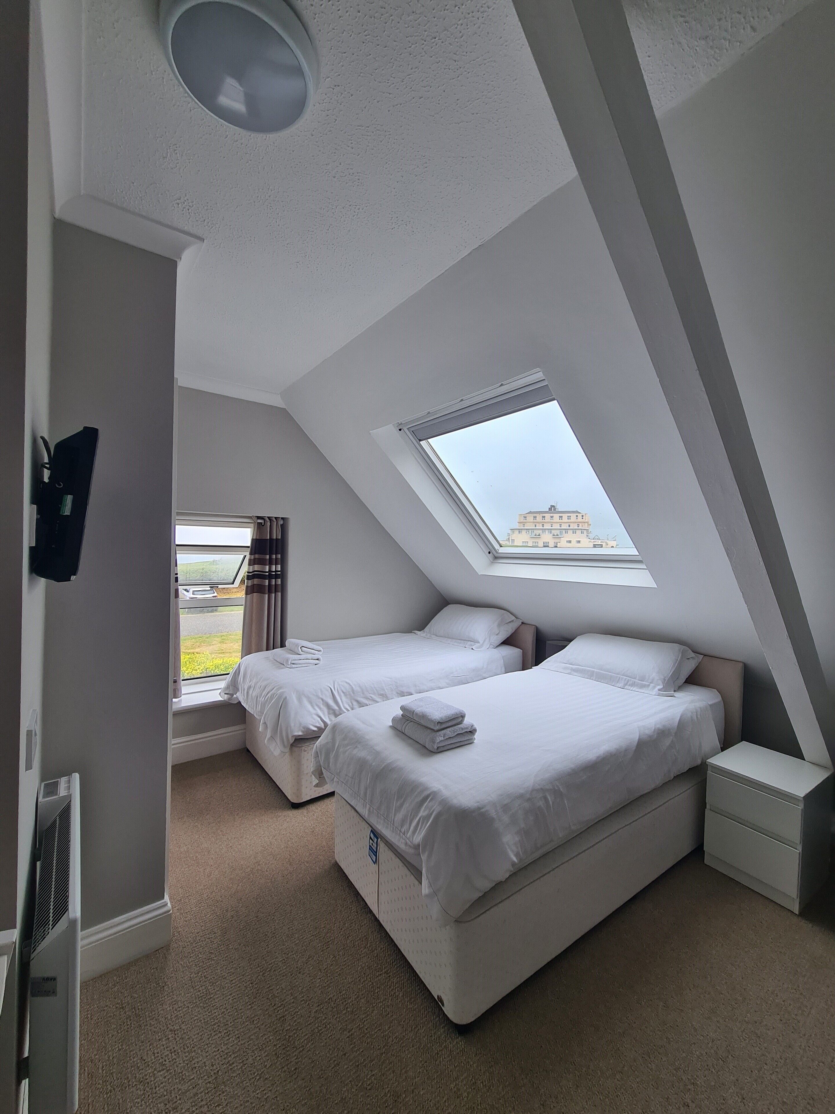 Une chambre avec deux lits, un puits de lumière, un radiateur et une fenêtre avec des rideaux.