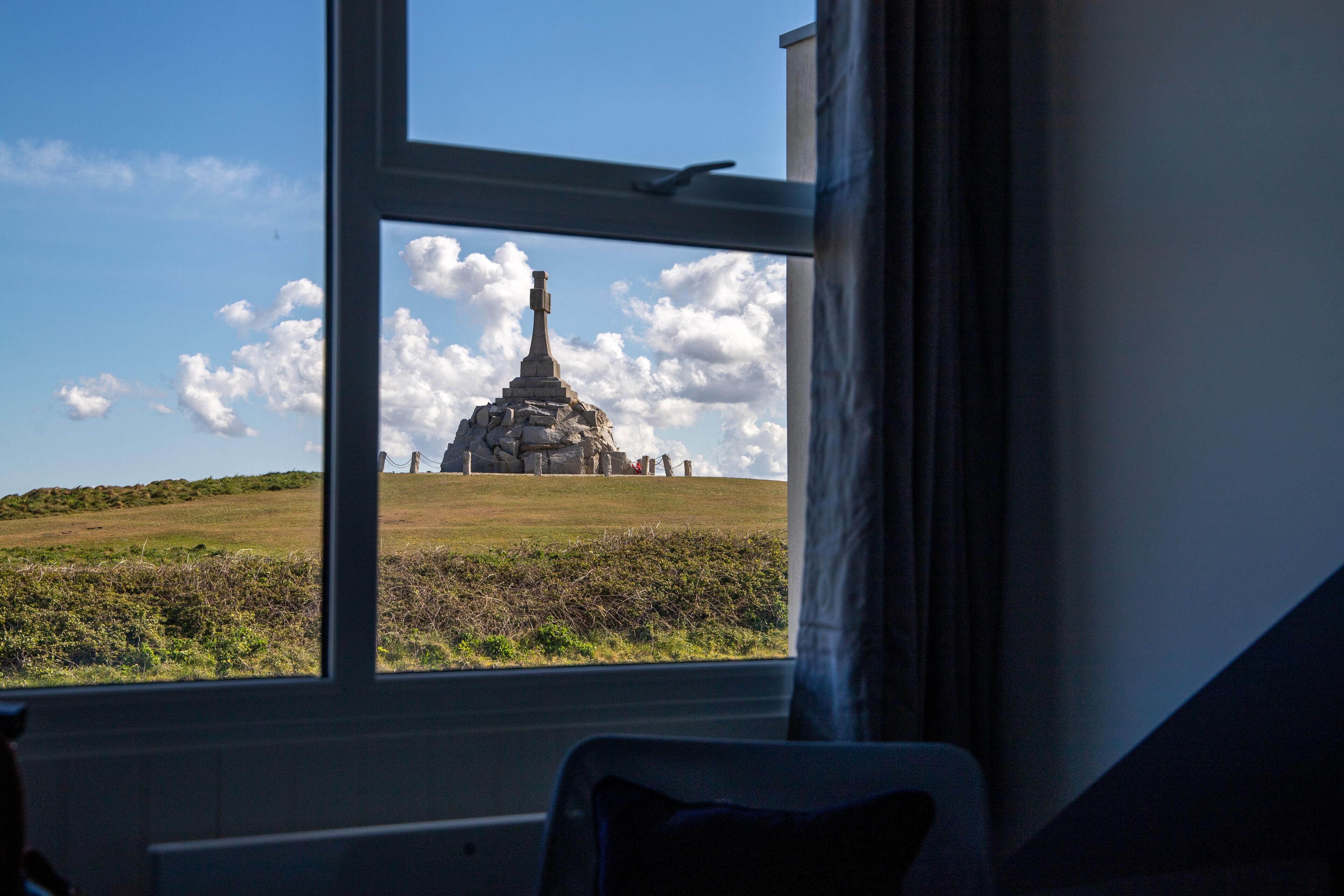 Vista a través de una ventana que muestra un edificio y un monumento de piedra en un campo.