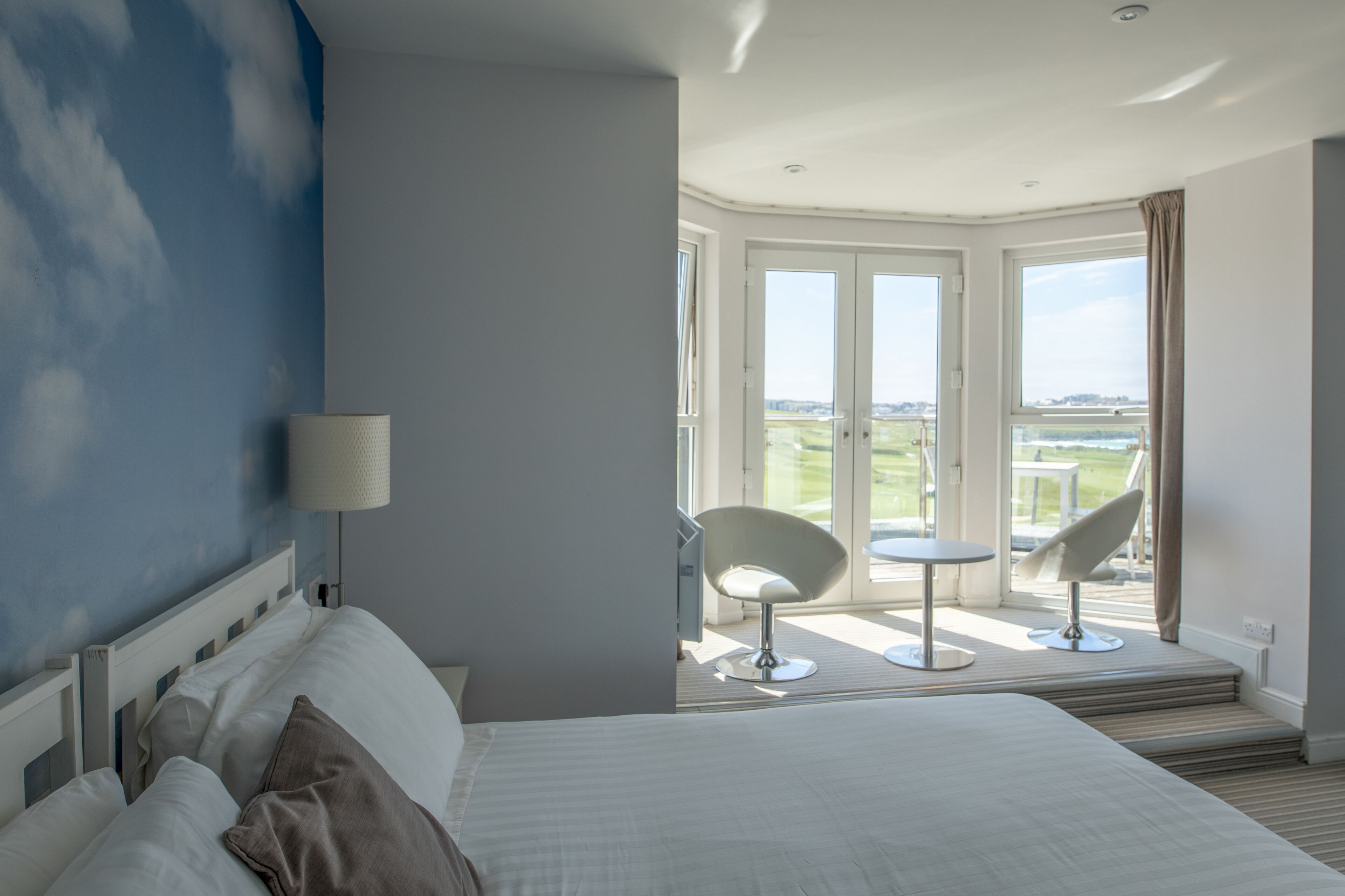 A hotel room with a bed, a chair, a small table, and a view of the outdoors.