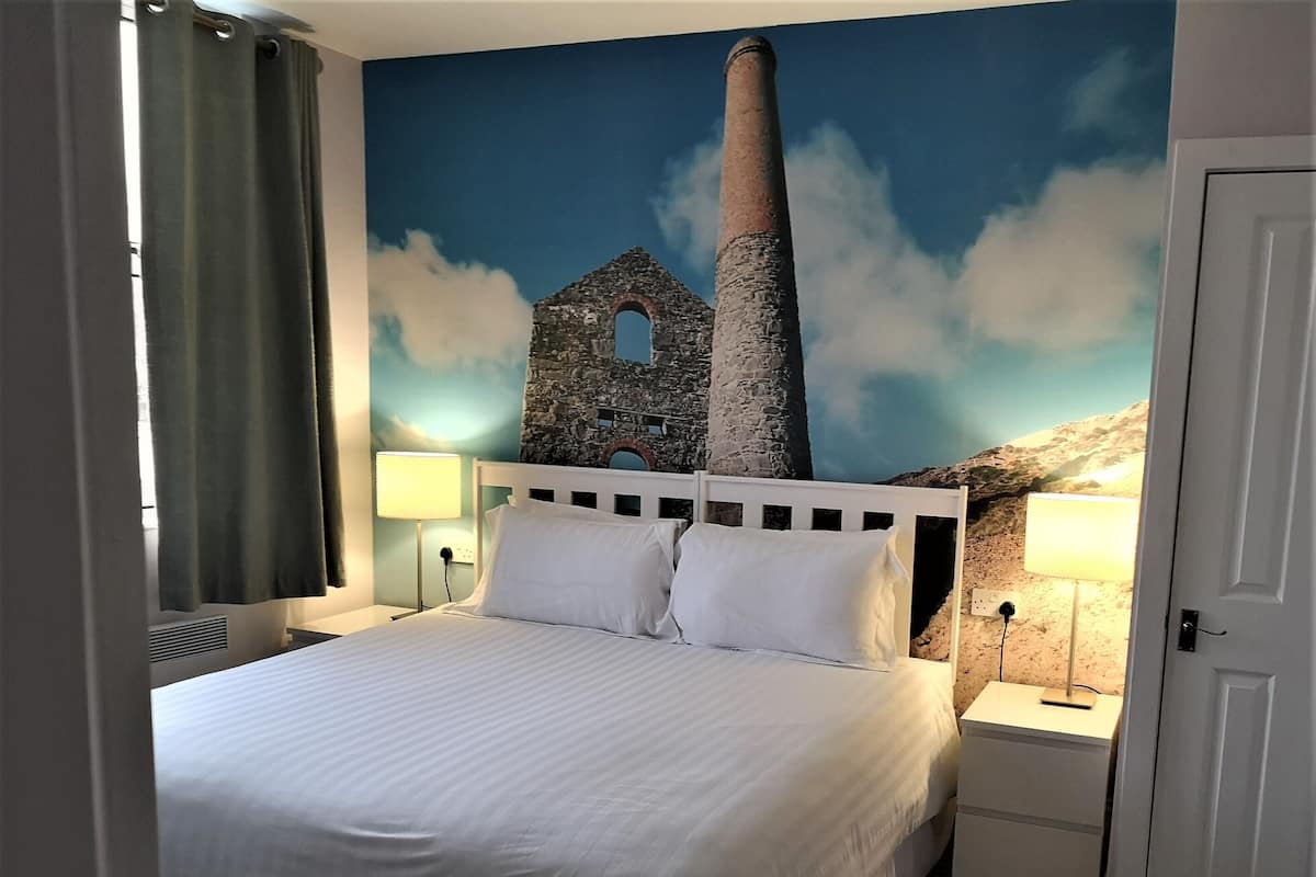 A hotel room with a large bed, two bedside tables, a wall mural, and a door.