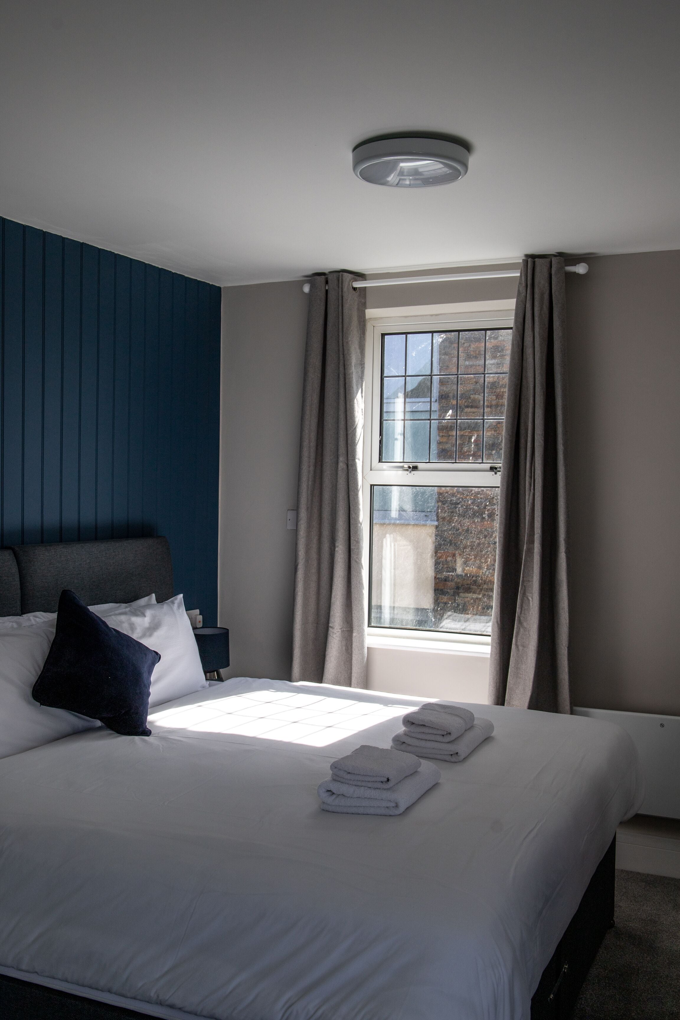 A hotel room with a bed, a nightstand, a window with curtains, and a ceiling light.