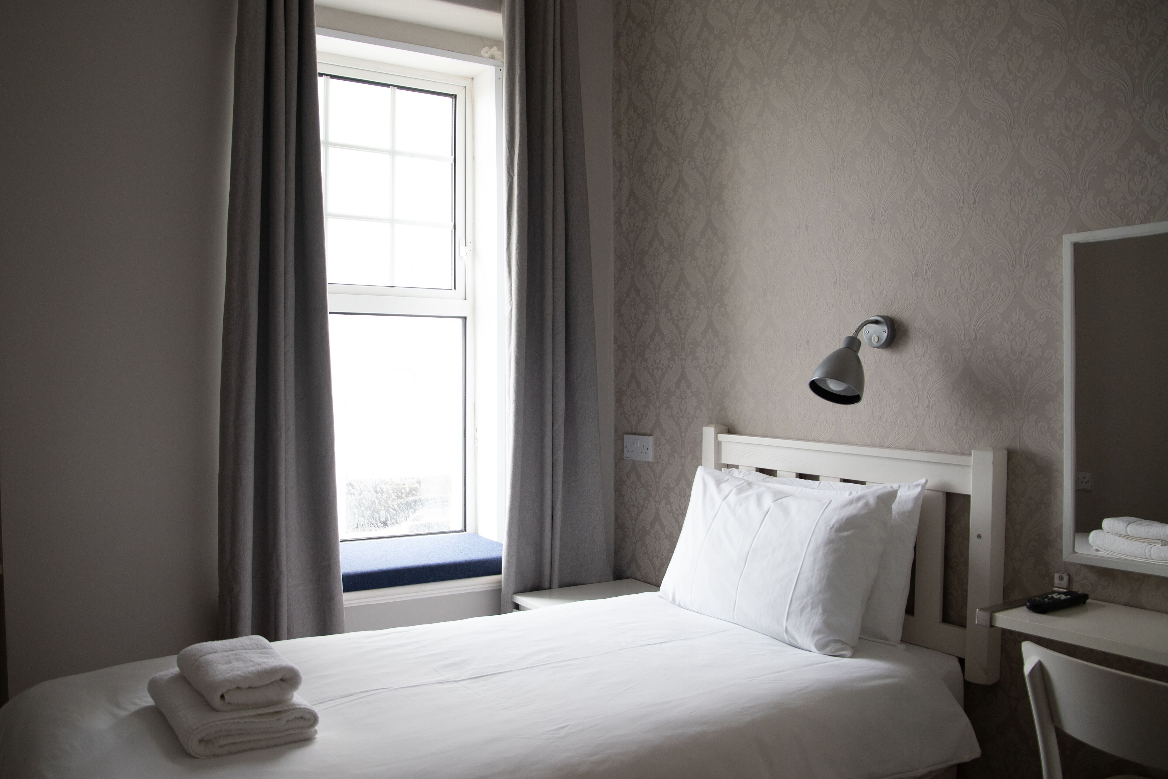 A hotel room with a bed, a desk, a lamp, and a window with curtains.