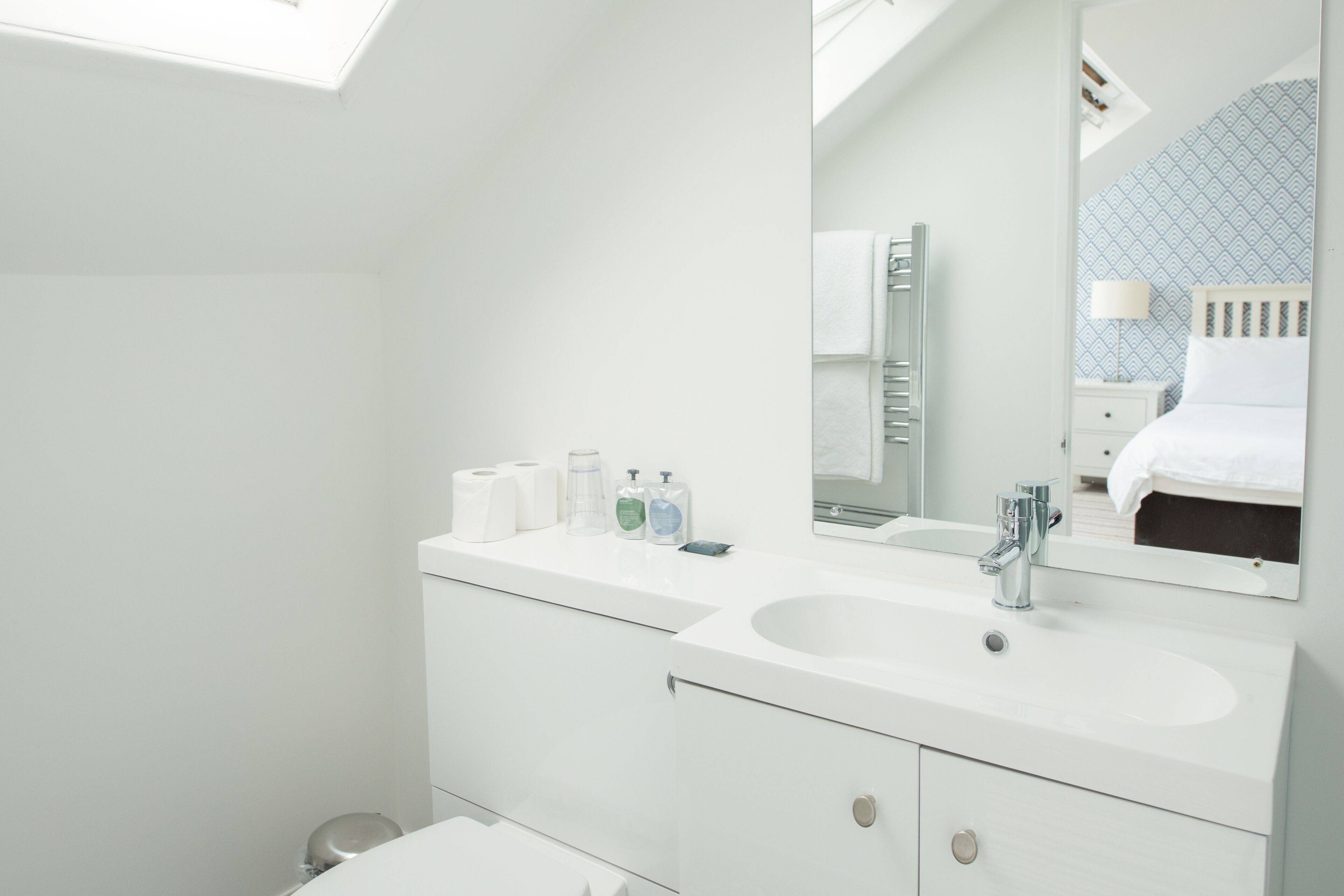 Un baño moderno con tragaluz, dos lavamanos y un espejo grande.