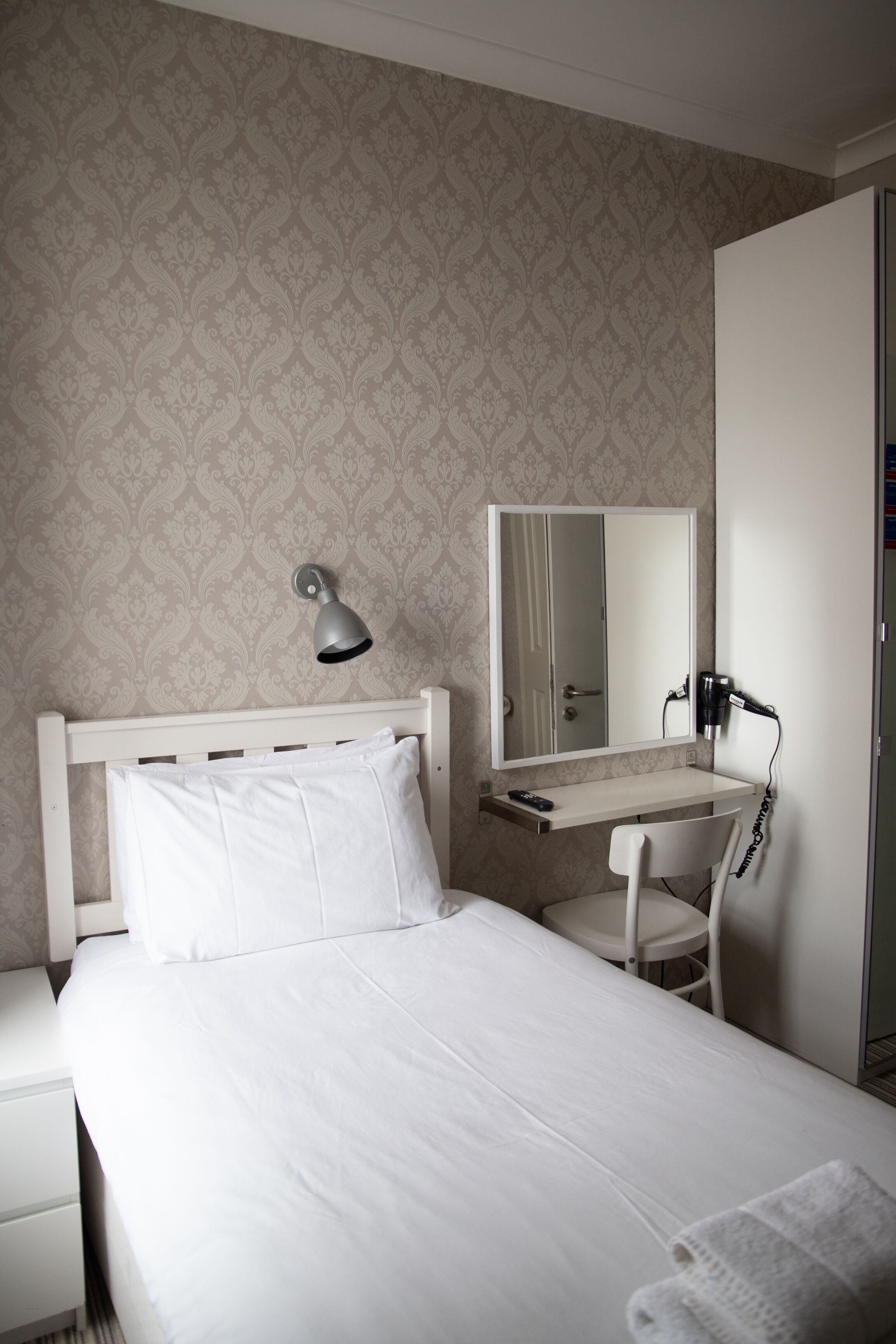 Quarto de hotel com uma cama, mesa de cabeceira, escrivaninha, cadeira, espelho e secador de cabelo.