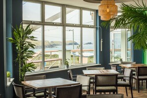 Un restaurante con amplios ventanales, mesas y sillas de madera, y vistas al mar.