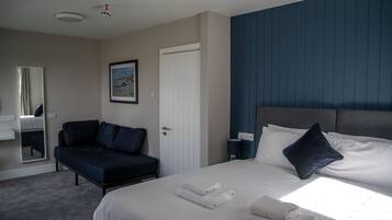 A hotel room with a bed, a sofa, a mirror, a painting, and a door.