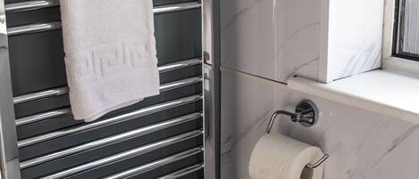 A bathroom with a chrome towel rack, a white towel, marble walls, and a toilet paper holder.