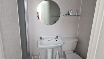 A compact bathroom with a white toilet, a pedestal sink, and a round mirror.